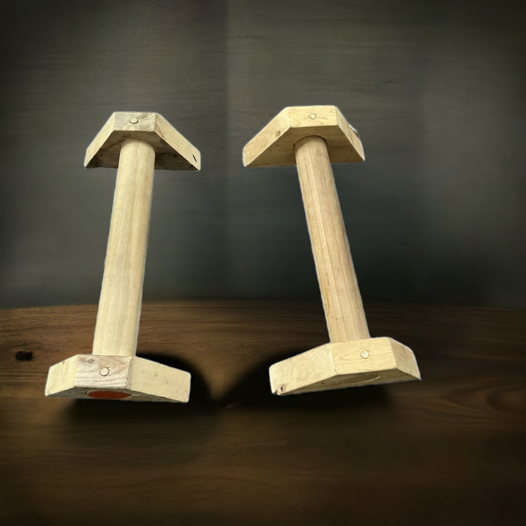 Hand-routed 2-inch thick wooden parallettes ( on a wooden surface with a dark background ) for grip strength training by Rough Road Fitness.