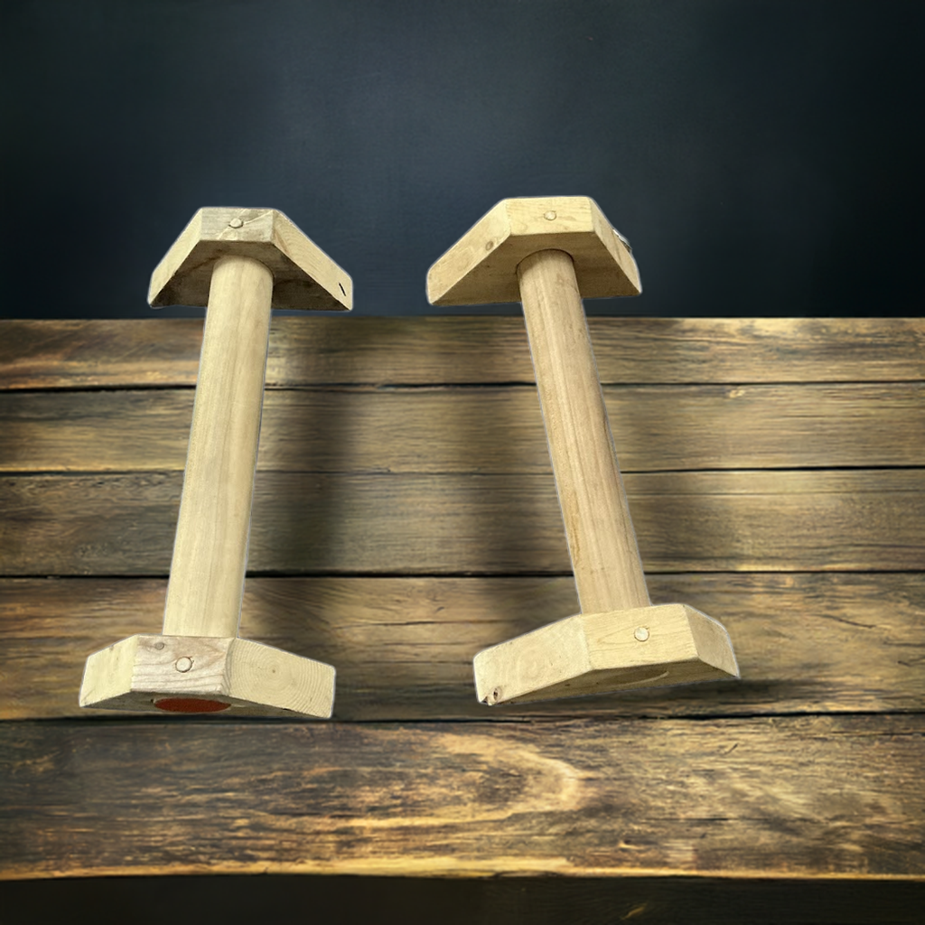 Hand-routed 2-inch thick wooden parallettes ( on a wooden floor with a dark background ) for grip strength training by Rough Road Fitness.