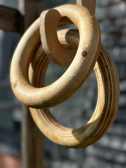 Hand-routed 3-inch thick wooden fitness rings on a wooden linking hook for grip strength training by Rough Road Fitness.